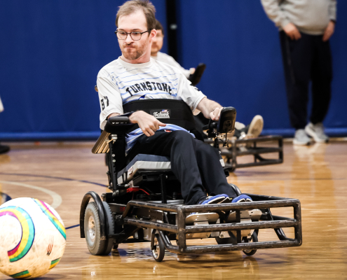 A man with a beard and glasses plays ball while using a wheelchair