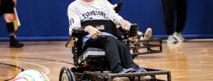 A man with a beard and glasses plays ball while using a wheelchair