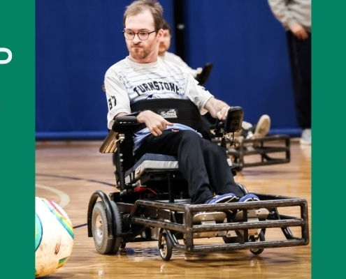 A man with a beard and glasses is playing ball while using a wheelchair