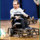 A man with a beard and glasses is playing ball while using a wheelchair